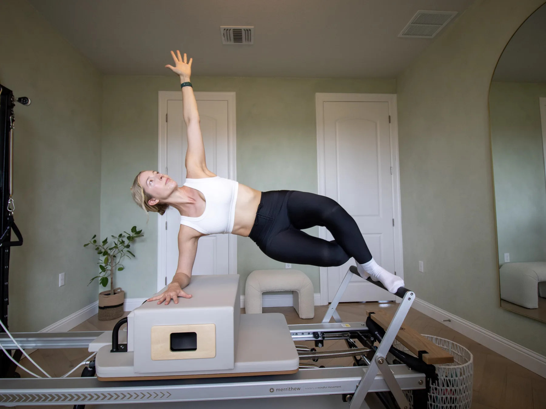 Courtney holding a side plank over the box on the Reformer, one arm reaching overhead